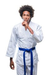 Afro american man wearing karate kimono over isolated background asking to be quiet with finger on lips. Silence and secret concept.