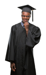 Young graduated african american man over isolated background with hand on chin thinking about question, pensive expression. Smiling with thoughtful face. Doubt concept.