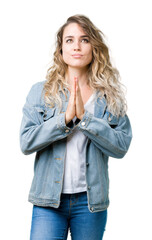 Beautiful young blonde woman wearing denim jacket over isolated background praying with hands together asking for forgiveness smiling confident.