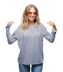Obraz premium Beautiful young blonde woman wearing sunglasses over isolated background looking confident with smile on face, pointing oneself with fingers proud and happy.