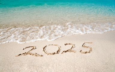 Top view of 2025 numbers written on the sand of coastline with frothy waves. 2025 new year concept.