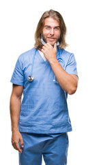 Young handsome doctor man with long hair over isolated background looking confident at the camera with smile with crossed arms and hand raised on chin. Thinking positive.