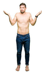 Handsome shirtless man showing nude chest clueless and confused expression with arms and hands raised. Doubt concept.