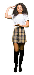 Young beautiful girl with curly hair wearing casual white t-shirt gesturing with hands showing big and large size sign, measure symbol. Smiling looking at the camera. Measuring concept.