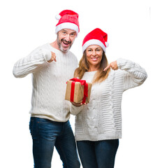 Middle age hispanic couple wearing christmas hat and holding gift over isolated background with surprise face pointing finger to himself