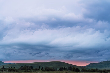 Obraz premium Green meadows and hills at sunset under the evening sky.