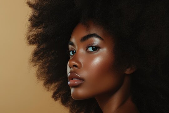 Young black model with afro hair nude make up and long dark hair against a beige backdrop