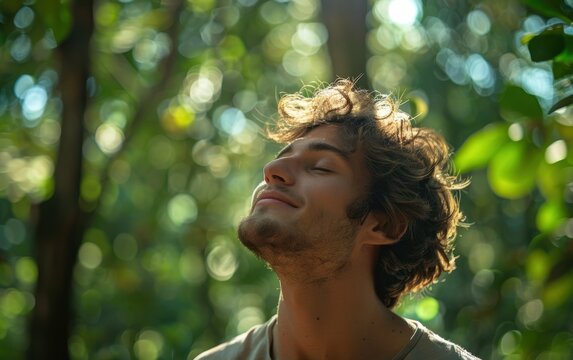 A young man with curly hair breathes deeply in a lush green forest on a sunny day