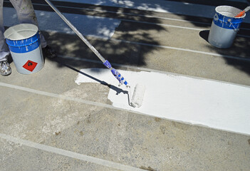 Pintor pintando sobre el asfalto un paso de peatones en la calle de la ciudad con rodillo y pintura blanca acrílica. Señalización de un paso de cebra.
