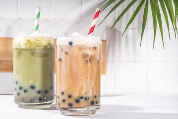 Classic and green matcha boba bubble tea with tapioca pearls and whipped non-dairy creamer on top of glass, summer cold sweet dessert drink on white table background copy space