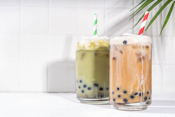 Classic and green matcha boba bubble tea with tapioca pearls and whipped non-dairy creamer on top of glass, summer cold sweet dessert drink on white table background copy space