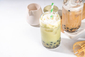 Classic and green matcha boba bubble tea with tapioca pearls and whipped non-dairy creamer on top of glass, summer cold sweet dessert drink on white table background copy space