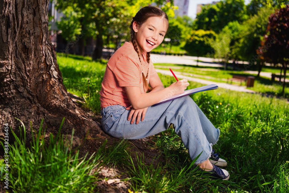 Wall mural full length photo of adorable little girl have fun outside activity sit under tree homework enjoy su