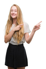 Obraz premium Blonde teenager woman wearing moles shirt smiling and looking at the camera pointing with two hands and fingers to the side.