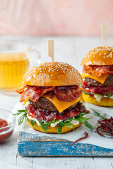 Big beef burger with onion marmalade, bacon, cheddar cheese, tomato and arugula on a wooden board
