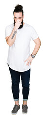 Young hipster man with long hair and beard wearing casual white t-shirt smelling something stinky...