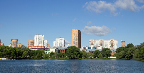 Beautiful panoramic landscape - modern high-rise buildings on the shore of a pond among the lush foliage of trees in Reutov, Moscow region on a clear summer sunny day