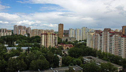 Obraz premium Cityscape - panoramic top view of a residential quarter with modern high-rise buildings with green trees on a sunny summer day and blue sky with white clouds in Reutov, Moscow region and copy space