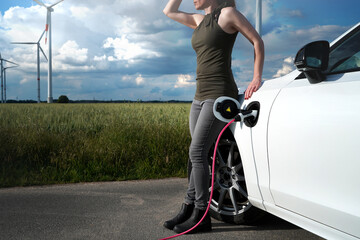 Beautiful woman in sleeveless top looks around in area with wind turbines while waiting that her...