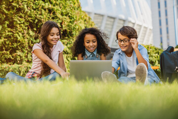 Low angle view of happy little preteen school children kids using digital wireless gadgets laptop...