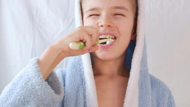 Portrait of a small child, a boy, in a blue robe brushing his teeth with a toothbrush on white, Healthcare, oral hygiene.