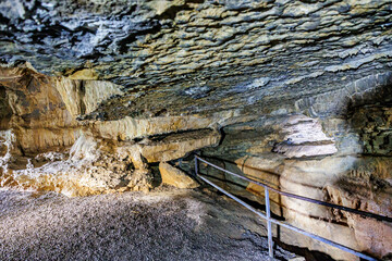 Fototapeta premium Underground cave in a rock formation with irregular, grooved ceiling and rock walls, illuminated with light lamps, below Logne Castle, summer day in Ferrieres, Belgium