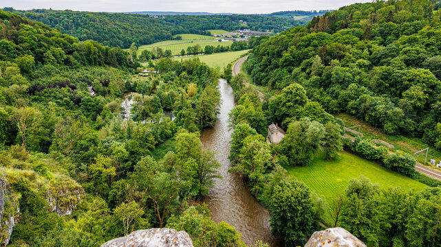 Valley with abundant green leafy trees and Ourthe river with abundant water slightly overflowing, mountains with horizon in background, seen from Logne castle, cloudy day in Ferrieres, Belgium