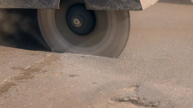 Pothole road repair. A close-up of a circular saw cutting a rectangle around a pothole in the road for replacement with new asphalt.