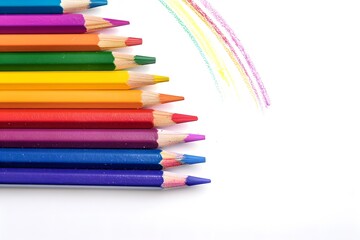Fototapeta premium Colored pencils and a drawn rainbow on a white background.