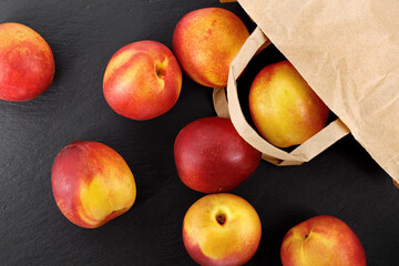 top view of nectarines tumbling out of a brown paper bag on black slate background