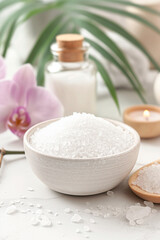 A bowl of salt is on a table with a candle and a vase of flowers