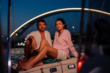 A couple enjoying a romantic evening on a boat under a bridge with city lights in the background.