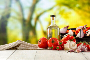 Olive oil and garlic and peppers and tomatoes and vegetables on wooden table top with space for advertised products and food. Summer grilling and good healthy food idea. Blur green garden background.
