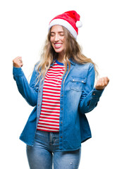 Beautiful young blonde woman wearing christmas hat over isolated background very happy and excited doing winner gesture with arms raised, smiling and screaming for success. Celebration concept.