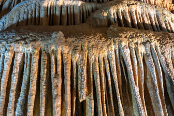 A detailed view of stalactites in a cave, characterized by elongated, drippy formations of limestone and mineral deposits hanging from the cave ceiling, showcasing the intricate of natural geology