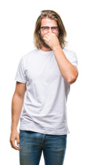 Fototapeta premium Young handsome man with long hair wearing glasses over isolated background smelling something stinky and disgusting, intolerable smell, holding breath with fingers on nose. Bad smells concept.