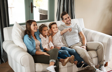 Parents, kids and watching tv on sofa with smile, point and relax together for bonding in family...