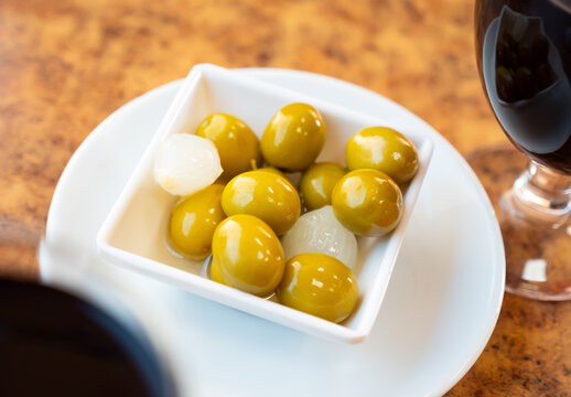 Savory pickled green olives, gherkins and pearl onions served with glass of wine. Traditional Mediterranean appetizer