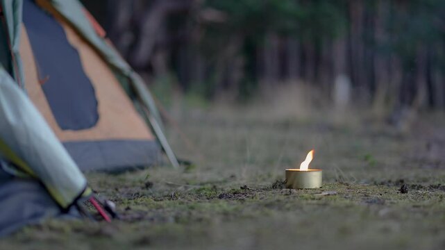 Mosquito repellent - citronella candle with flame near camping tents in forest. Lighted candle with lemongrass to prevent mosquito bites. Perfect for windless summer evenings outdoors.