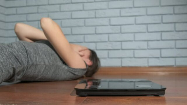 Teen anorexia problems. A teen girl with anorexia problems crying by the smart scales on the floor indoor.