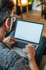 Closeup of man working on laptop with a white screen mock up on sitting on a sofa at home