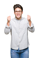 Young handsome man wearing glasses over isolated background excited for success with arms raised celebrating victory smiling. Winner concept.