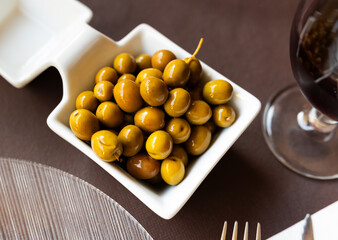 White bowl filled with marinated green olives as tangy and savory snack for wine. Mediterranean gastronomic culture