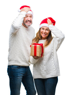 Middle age hispanic couple wearing christmas hat and holding gift over isolated background stressed with hand on head, shocked with shame and surprise face, angry and frustrated. Fear and upset.