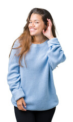 Young beautiful brunette woman wearing blue winter sweater over isolated background smiling with hand over ear listening an hearing to rumor or gossip. Deafness concept.