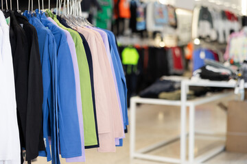 Sweatshirts of different colors hang on hangers on rack in clothing store