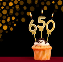 Number 650 birthday candle - Cupcake on black background with out of focus lights