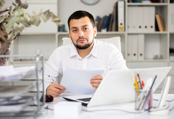 Fototapeta premium Caucaisan businessman doing his daily work in office. Cheerful man sitting at desk and working.