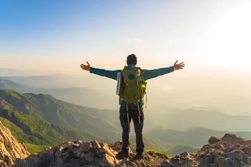 Mountaineer with backpack on shoulders on top of mountain with arms outstretched, travel,...