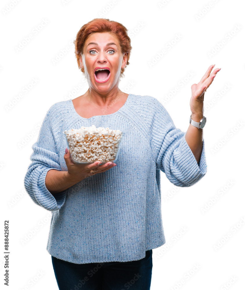 Sticker Atrractive senior caucasian redhead woman eating popcorn over isolated background very happy and excited, winner expression celebrating victory screaming with big smile and raised hands